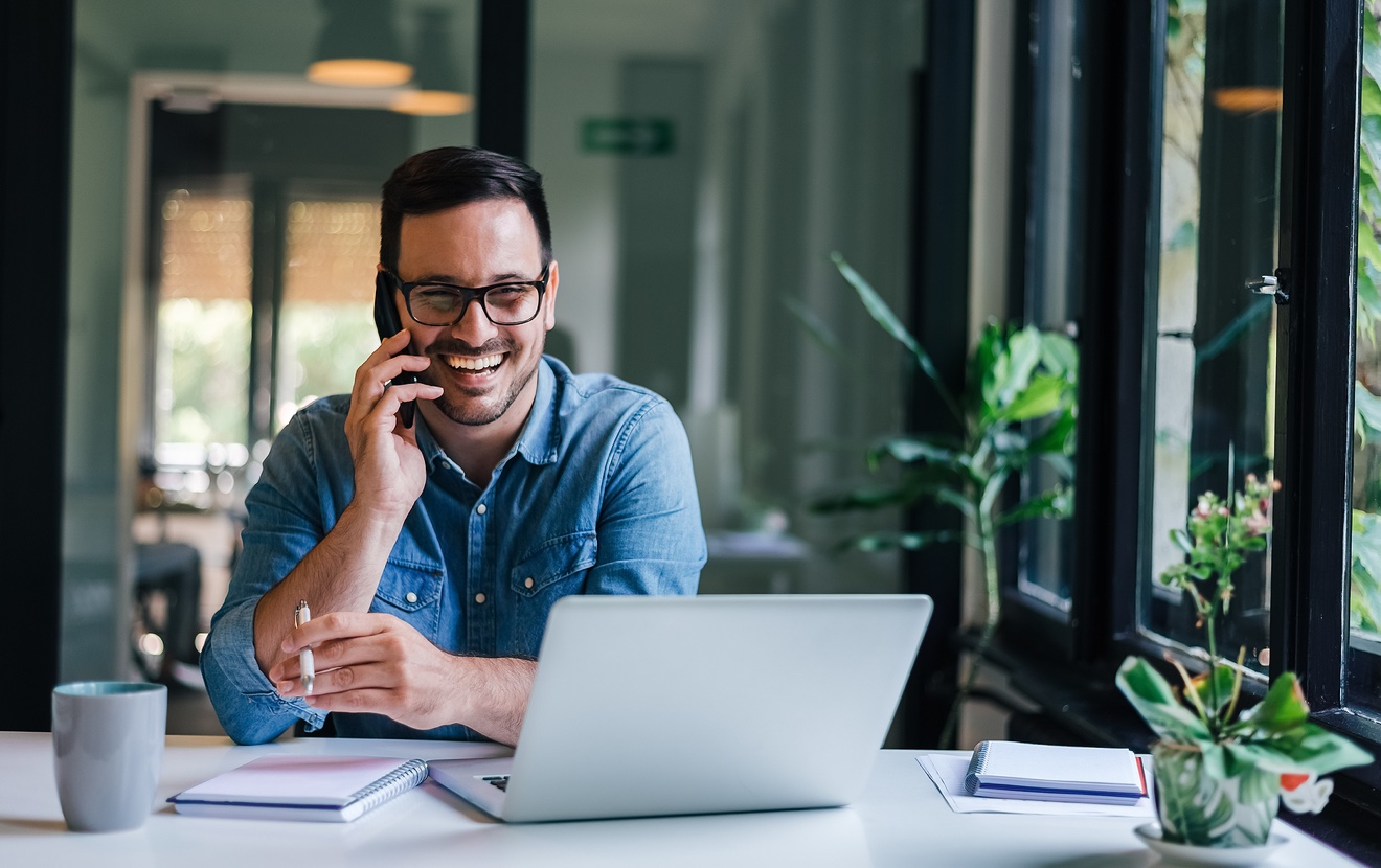Portrait Of Young Smiling Cheerful Entrepreneur In Casual Office Making Phone Call While Working Wit
