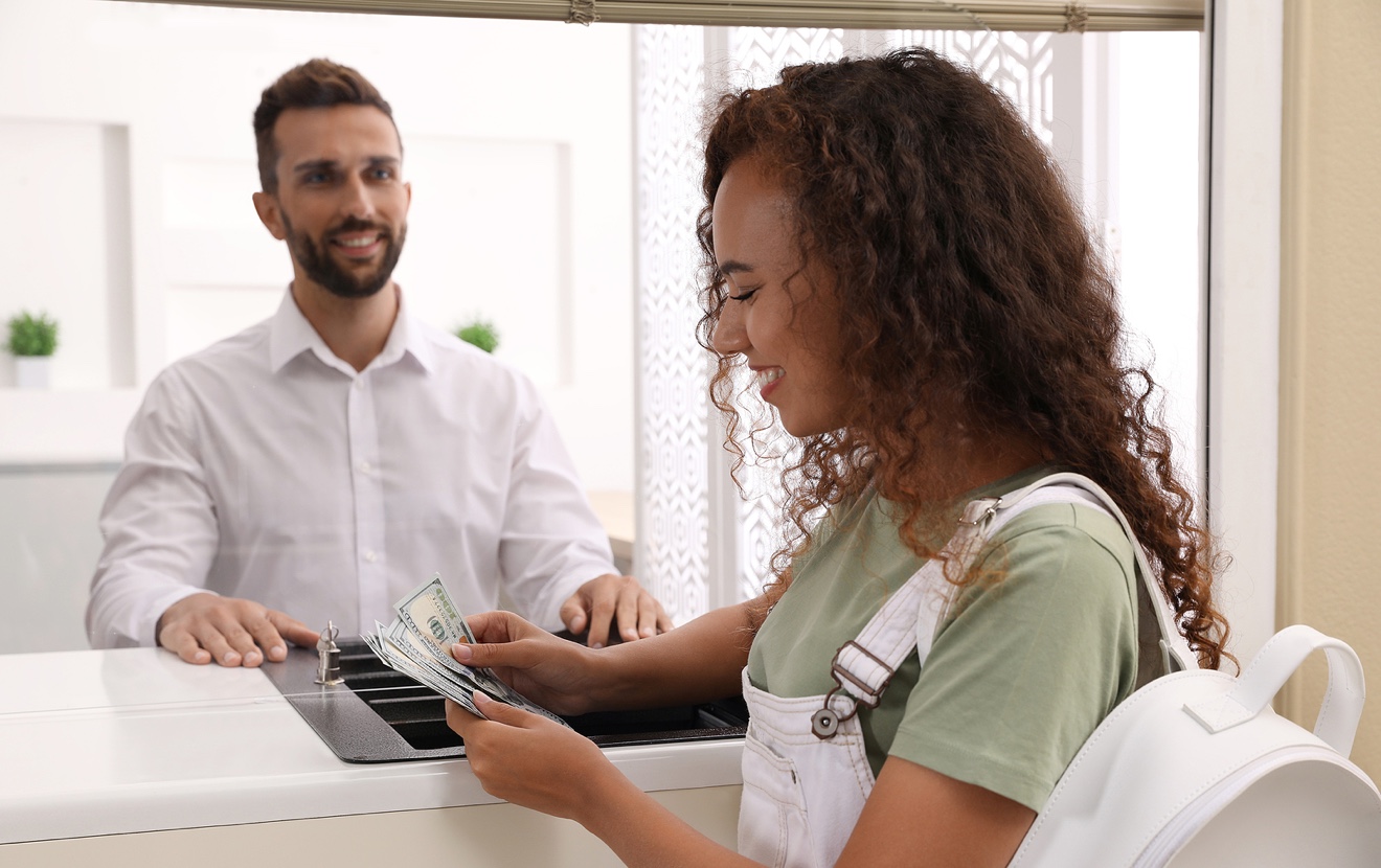 African American Woman With Money At Cash Department Window In Bank. Currency Exchange